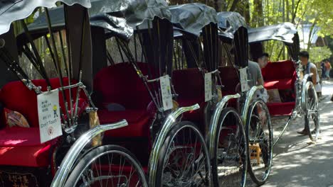 Rickshaw-Estacionado-En-Una-Fila-En-El-Bosque-De-Bambú-En-Kyoto,-Sol-De-Mediodía-De-Japón-Cámara-Lenta-4k