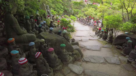 Small-Buddha-statues-with-woolly-hat-on-a-path-of-the-Daisho-in-Buddhist-temple-site-on-the-on-Miyajima-Island,-prefecture-of-Hiroshima