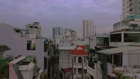Before-dawn-descending-dolly-drone-shot-with-view-of-alleyway-in-densely-populated-residential-area-in-Southeast-Asia-featuring-traditional-buildings,houses,-catholic-church-and-high-rise-buildings