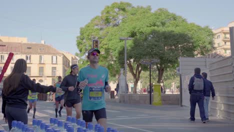 Toma-En-Cámara-Lenta-Del-Corredor-Tomando-Una-Botella-De-Agua-Del-Punto-De-Dispensación-De-Agua-De-Maratón,-Málaga,-Centro-De-La-Ciudad