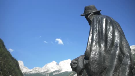 Black-statue-of-mountaineer-and-botanist-Julius-Kugy-looking-towards-snowy-mountains-on-sunny-summer-day