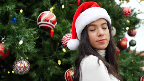 Attractive-woman-in-a-Santa-hat-celebrating-the-holiday-season-with-a-Christmas-tree-ornaments-and-lights