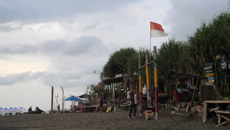 Strandverkäufer-Unterhalten-Sich-Auf-Bali,-über-Ihnen-Weht-Eine-Indonesische-Flagge