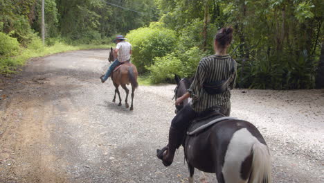 Slow-motion-back-shot-of-young-couple-horseback-riding-through-the-forest-pathway-in-Nosara,-Costa-Rica