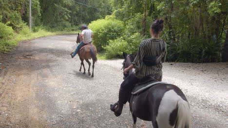 Toma-En-Cámara-Lenta-De-Una-Pareja-Joven-Montando-A-Caballo-Por-El-Sendero-Del-Bosque-En-Nosara,-Costa-Rica