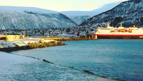 Gran-Barco-De-Pasajeros-Que-Llega-Al-Puerto-En-Un-Lago-Natural-En-Tromso-Noruega-Con-La-Montaña-Cubierta-De-Nieve-En-El-Fondo