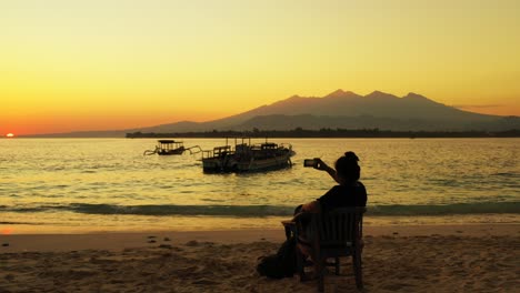 Isla-De-Samar,-Filipinas---Mujer-Turista-Sentada-En-La-Silla-De-Madera-En-La-Playa-Mientras-Observa-La-Hermosa-Puesta-De-Sol---Gran-Plano