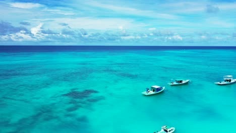 Kleine-Boote-Schwimmen-über-Einer-Ruhigen-Türkisfarbenen-Lagune-Mit-Klarem-Wasser-Und-Korallenriffmustern,-Die-Von-Tiefblauem-Ozean-Unter-Hellem-Himmel-Mit-Wolken-In-Jamaika-Begrenzt-Werden
