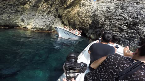 Boat-exits-narrow-cave-opening-in-rocky-cliff-while-passengers-in-another-boat-wave-and-wait-to-enter