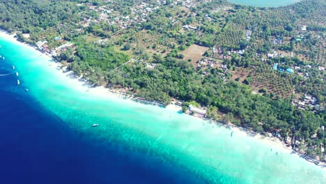 Deep-blue-sea-next-to-turquoise-shallow-lagoon-around-tropical-island-in-Gili-meno,-Indonesia-with-white-sandy-beach-and-hotels-inside-trees-forest