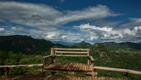 clouds-moving-over-wooden-bench-in-lush-green-mountainous-scenery,-time-lapse