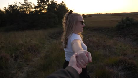 Young-happy-blonde-woman-takes-hand-from-boyfriend-and-smiles,-enjoying-the-sunset,-while-it-is-golden-hour,-medium-shot