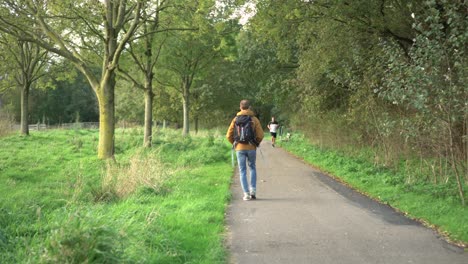 Man-walking-through-park-on-pathway-in-countryside-woods,-rear-view