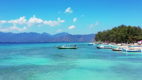 Boote-Ankern-Am-Ufer-Einer-Tropischen-Insel-Mit-Weißem-Sandstrand,-Umspült-Von-Ruhigem,-Klarem-Wasser-Der-Blau-türkisen-Lagune-An-Einem-Hellen-Himmel-In-Bali
