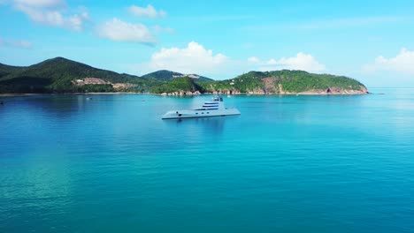 Luxurious-yacht-floating-on-blue-azure-sea-water-near-coastline-of-tropical-island-with-lush-vegetation-on-a-sunny-summer-day-in-Thailand