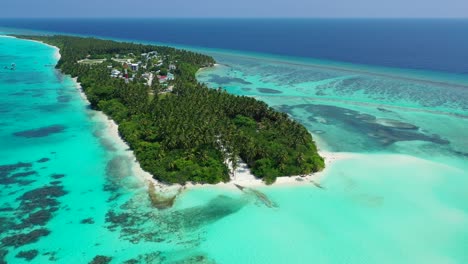 Vacation-resort-situated-inside-palm-trees-forest-of-tropical-island-surrounded-by-calm-clear-water-of-turquoise-lagoon-with-coral-reef-and-white-sand-in-Fulhadhoo,-Maldives
