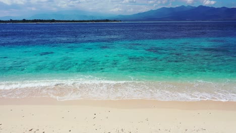 Lebendige-Farben-Des-Meeres-Mit-Blau-türkiser-Lagune-Und-Weißen-Wellen,-Die-Den-Sand-Eines-Exotischen-Strandes-An-Einem-Hellen-Sommertag-Mit-Bewölktem-Himmel-In-Indonesien-Umspülen