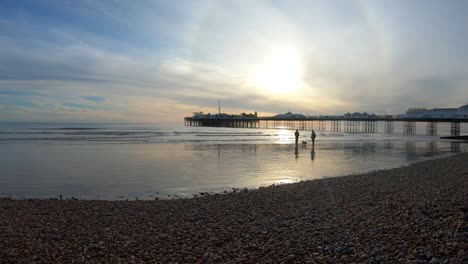 Beach-timelapse-at-sunset-with-people-playing-in-the-water,-sun-flare-and-pier