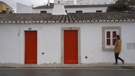 Frau-Geht-Vor-Einem-Traditionellen-Haus-Mit-Roter-Tür-In-Tavira,-Algarve,-Portugal-Vorbei