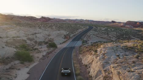 Black-Ferrari-driving-down-an-open-highway-in-the-Valley-of-Fire,-Nevada,-at-sunset