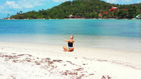 Happy-woman-with-a-big-smile-practicing-yoga-and-meditating-on-the-sandbar-in-Thailand