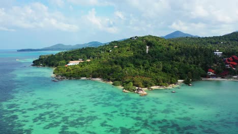 Aerial---lush-tropical-forest-on-the-island-hill-with-luxury-resorts-surrounded-by-crystal-clear-turquoise-sea-water