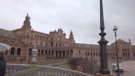 Touristen-Mit-Sonnenschirmen-Am-Verregneten-Plaza-De-Espana-In-Sevilla,-Spanien,-Schwenk-Nach-Rechts