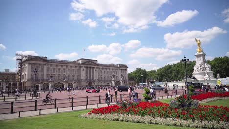Buckingham-Palace-in-London-with-walking-people-and-red-flowers-in-garden,-sunny-day,-wide-angle-static-shot