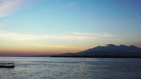 Wunderschöne-Dämmerungsfarben-Des-Hellen-Himmels-über-Der-Silhouette-Des-Berghorizonts,-Der-Sich-Auf-Der-Ruhigen-Meeresoberfläche-Spiegelt,-Wo-Boote-Schwimmen,-Bali
