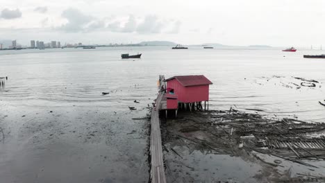 Brauner-Steg-Im-Meer-Mit-Fischerhütten-Und-Booten-In-Einem-Einkommensschwachen-Viertel-Der-Stadt-Bei-Ebbe,-Luftaufnahme-Eines-Drohnenüberflugs