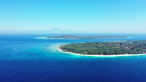 Blue-azure-sea-around-beautiful-tropical-island-with-trees-forest-and-white-sandy-beach-under-clear-bright-sky-in-Indonesia