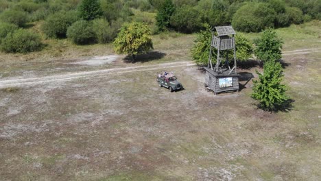 Aerial-View-of-Off-Road-Vehicle-Pulling-Up-To-Old-Wooden-Watch-Tower-Surrounded-by-Nature