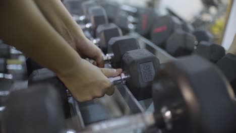 Female-hand-picks-up-dumb-bells-in-gym-for-training-and-exercise-for-body-building-and-reducing-weight,-Closeup-woman-hands-taking-weight-lifting-in-sport-club,-slow-motion