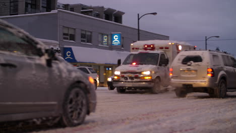 Ambulance-with-Sirens-Driving-Through-Traffic-on-Snowy-Street-during-rush-hour-at-dusk