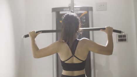 Backside-of-fitness-girl-working-out-at-gym-using-lat-pulldown-equipment-or-machine,-slow-motion