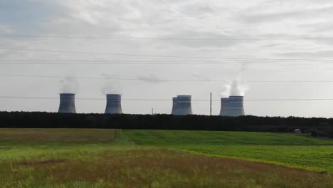 Luftbildverfolgung-Durch-Grüne-Felder-Mit-Modernem-Kernkraftwerk-über-Bäumen-Im-Hintergrund-Und-Elektrischen-Leitungen-Im-Vordergrund-In-Der-Ukraine