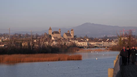 Rapperswil-Schlossfassade-Mit-Menschen,-Die-Auf-Einer-Fußgängerbrücke-Am-See-Vorbeigehen,-Weitwinkelaufnahme