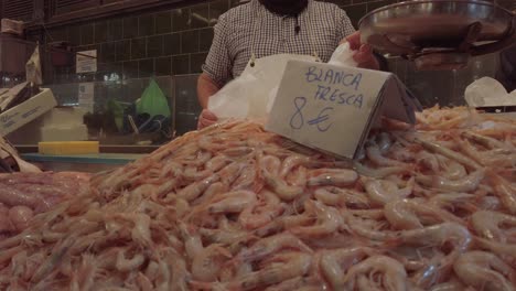 Heap-of-fresh-white-shrimp-at-market-with-vendor-in-background,-Slowmo-Close-Up