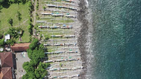 Amed-beach-in-Bali-Indonesia-with-Jukung-fishing-boats-lined-up-on-the-shore,-Aerial-top-view-pan-down-shot