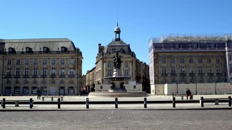 Place-de-la-Bourse-with-cars-passing-and-a-few-people-on-nearly-empty-square-due-to-the-COVID-19-pandemic,-Stable-handheld-shot