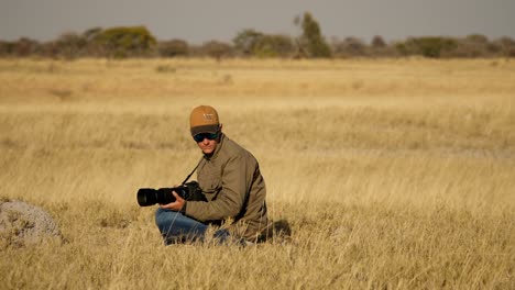 Ein-Professioneller-Naturfotograf-Sitzt-Im-Hohen-Gras,-Während-Ein-Erdmännchen-In-Der-Nähe-Nach-Nahrung-Sucht