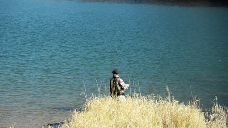 Man-walking-along-the-shore-of-an-lake-searching-for-a-fishing-sport