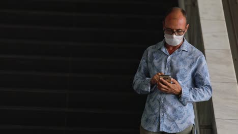 Brasilianischer-Mann,-Der-Eine-Medizinische-Gesichtsmaske-Trägt,-Tippt-Auf-Seinem-Telefon