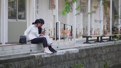 Japanese-Couple-Looking-At-The-Smart-Phone-Together-While-Sitting-In-Kyoto,-Japan---Wide-Shot
