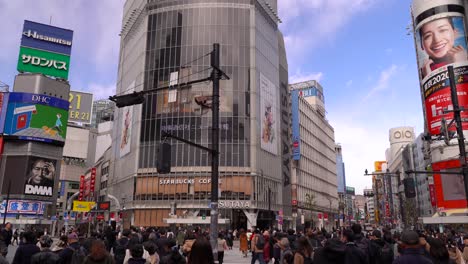 Gente-Cruzando-En-El-Carril-Peatonal-En-La-Intersección-En-Shibuya-Tokyo-Japón-Durante-El-Día-Con-Edificios-Comerciales-Y-De-Negocios-En-El-Fondo---Tiro-Medio