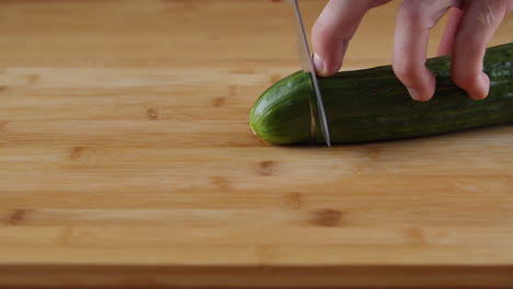 Hands-Slicing-A-Green-Cucumber-On-The-Chopping-Board-With-A-Knife---close-up