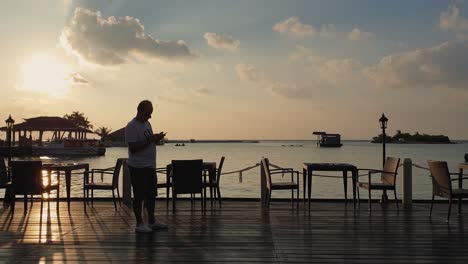 Männlicher-Tourist-Auf-Dem-Smartphone-In-Der-Abenddämmerung-Im-Restaurant-Im-Freien-Auf-Den-Malediven