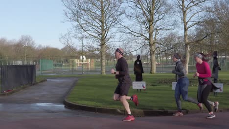 Active-fitness-group-walking-and-jogging-in-wet-rainy-park-in-slow-motion-side-parallax-tree-view