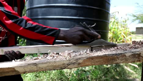 Kenyan-carpenter-working-outside-on-a-project-using-hand-tools-to-shave-and-shape-a-board-for-a-furniture-build