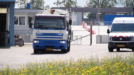 Garbage-truck-driving-near-yellow-flower-field-in-summer